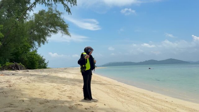 A young woman on the beach is preparing to go swimming with snorkeling gear on a sunny day
