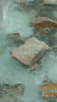 Turquoise glacial waters rush over rocks in soft natural light. Time-lapse photography, with cool tones predominating. Ideal for themes related to nature, adventure, and environmentalism