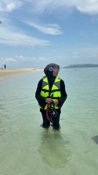 A young woman on the beach is preparing to go swimming with snorkeling gear on a sunny day