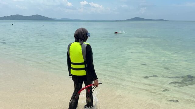 A young woman on the beach is preparing to go swimming with snorkeling gear on a sunny day