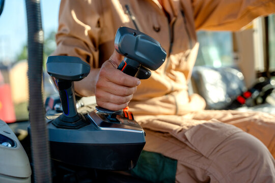 Operator controls equipment with joysticks during daytime work in an agricultural setting