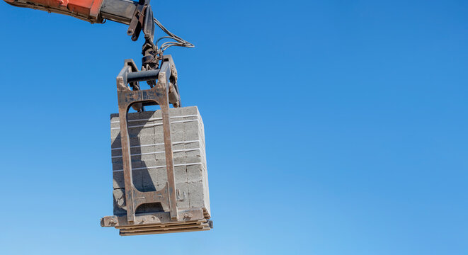 Construction crane lifts a large concrete block in clear blue sky at a building site during daytime hours