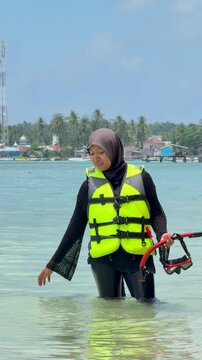 A young woman on the beach is preparing to go swimming with snorkeling gear on a sunny day