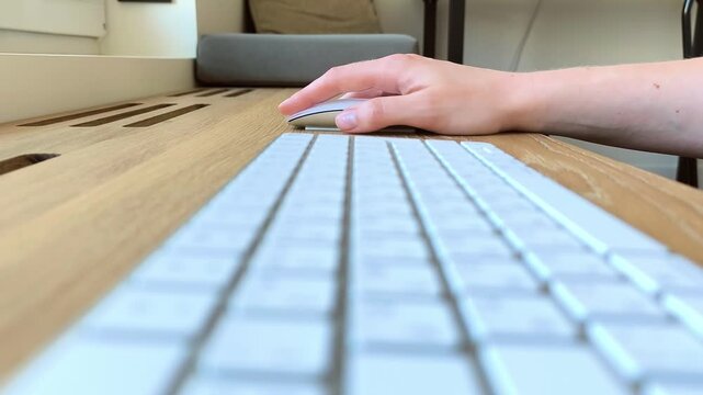 Side view of a hand moving a computer mouse. Keyboard positioned nearby during everyday navigation and scrolling. Close-up scene of office equipment in use..