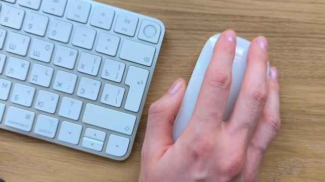 Top view of a hand clicking and scrolling a mouse. Keyboard visible nearby during overhead computer navigation. Close-up office scene captured from directly above..