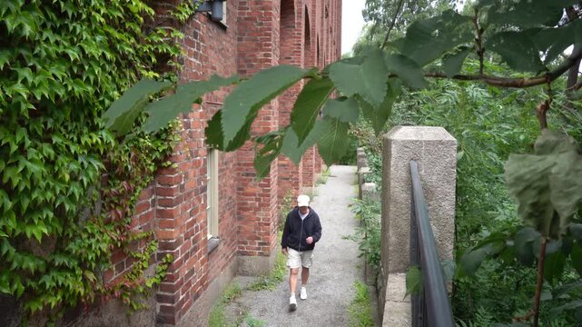 Stockholm, Sweden A man walks on a narrow path between brick buildings with ivy and greenery.