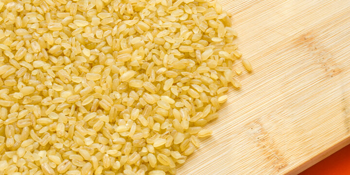 Heap of raw dry bulgur wheat groats poured on a light wooden board over a red background