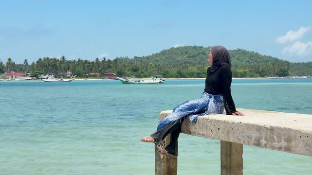A young woman sits on a beach pier in Kotabaru, gazing out at the sea