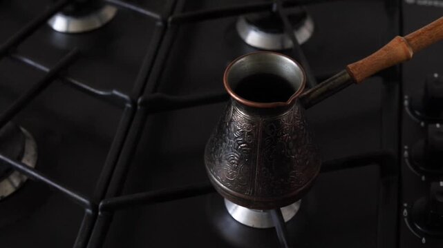 Making coffee in a cezve on a gas stove. Hand pours ground coffee into the cezve, adds water, and lights the gas burner.
