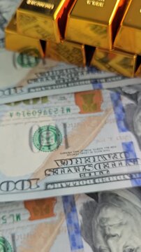 Gold bars and hundred dollar bills are stacked on a flat surface in a detailed display of wealth