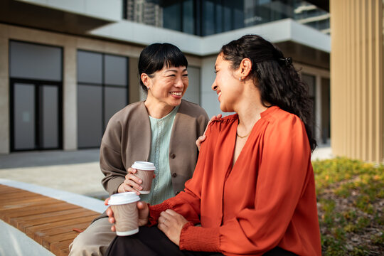 Two women sharing coffee on a city bench