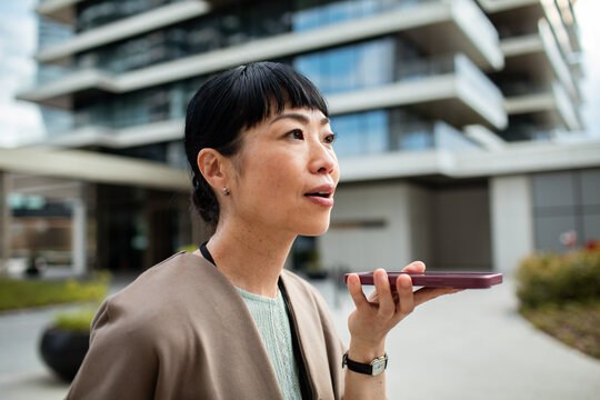 Woman using voice assistant on smartphone outside modern building