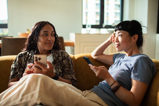Two friends chatting on a sofa at home with smartphones