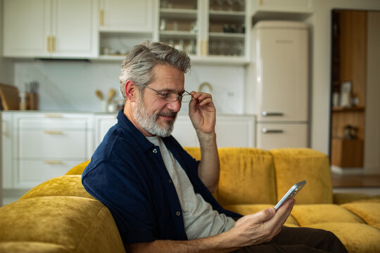 Middle-aged man using smartphone on sofa at home