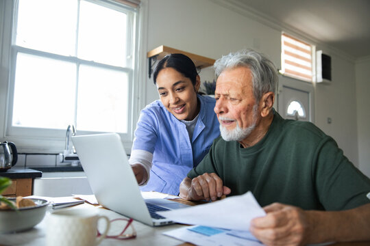 Home caregiver assisting elderly man on laptop in kitchen