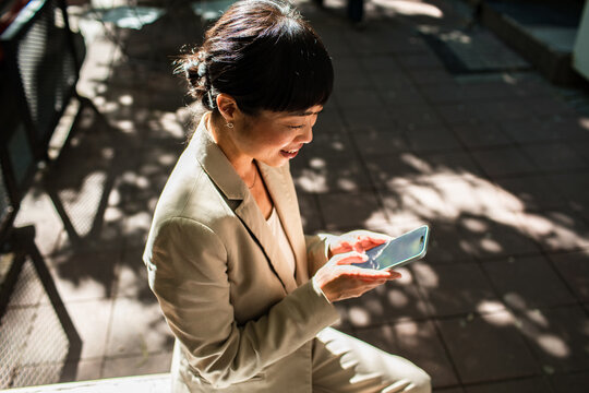 Smiling businesswoman using smartphone on sunny city sidewalk