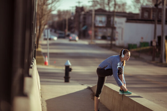 Woman runner tying shoelaces on urban street at sunrise