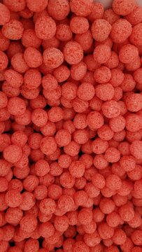 Full frame close-up view of bright red crunchy corn balls or puffed cereal snacks.
