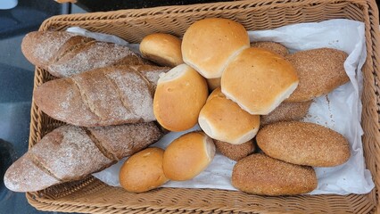 Naklejka premium Top view of an assortment of freshly baked bread loaves and rolls neatly arranged in a woven basket.