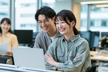 Fototapeta premium オフィスで笑顔でノートパソコンを見つめる若い日本人ビジネスマンと女性