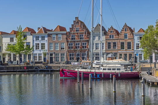 Goes, Netherlands - April 22, 2026: A vibrant magenta sailboat docked at the historic city harbor Stadshaven against a backdrop of classic gabled Dutch houses.