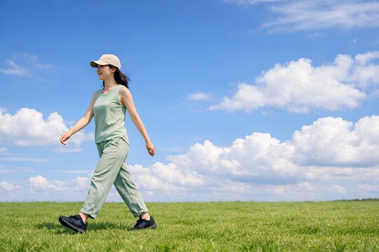 青空広がる芝生で気持ちよくウォーキングする若い女性の健康的な姿