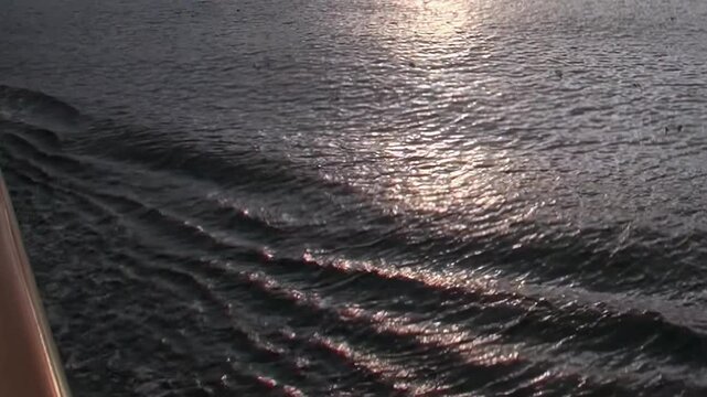 Glimpse the Arctic Ocean's surface as sunlight glistens, creating a radiant path on dark water. Gentle waves and ship's wake show the vessel's steady progress through polar waters.