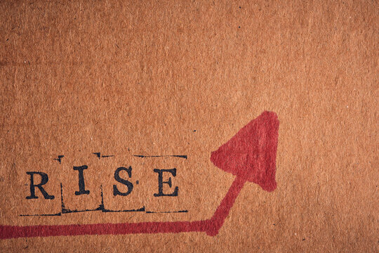 Stamped word RISE with bold red arrow pointing up on textured brown cardboard, macro shot.