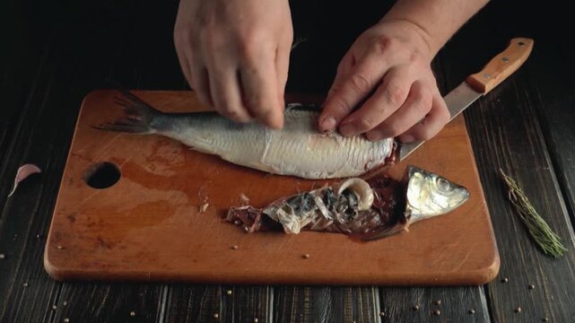 Hands of a male chef skillfully filleting a fresh fish on a wooden cutting board, with a sharp knife and scattered spices visible in a well-lit kitchen setting