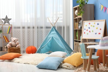 Blue wigwam, colorful pillows, poufs and shelving units in stylish child's room. Interior design © New Africa