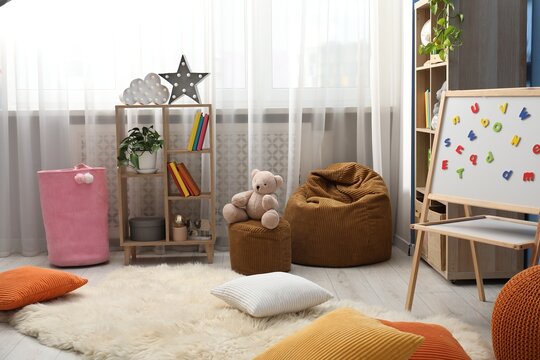 Shelving units, colorful pillows, poufs and magnetic board in stylish child's room. Interior design
