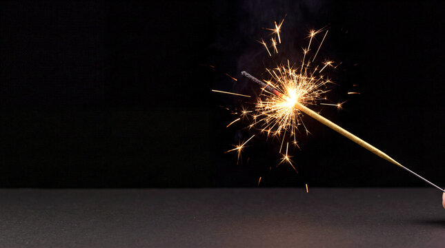 Burning sparkler on black background. Bright firework stick for birthday or holiday party.