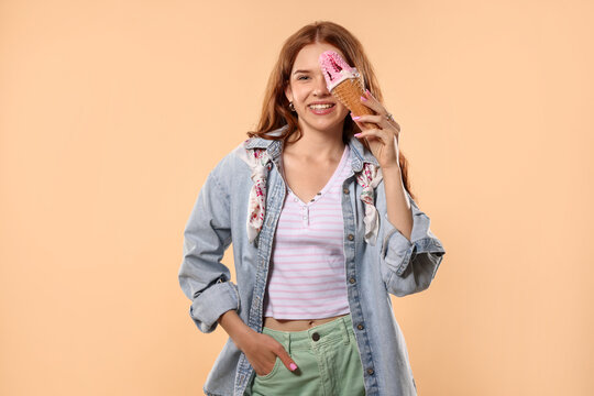 Happy teenage girl with delicious ice cream in waffle cone on beige background