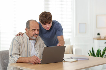 Fototapeta premium Caregiver. Teenager helping senior man learn how to use laptop indoors, space for text