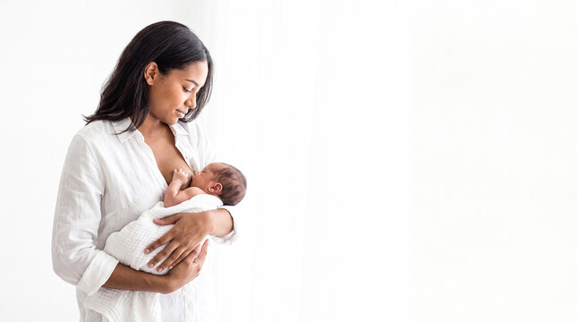 Mother breastfeeding newborn baby. Young woman nursing infant in a white studio setting.