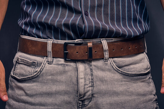 Midsection shot man wearing grey jeans, brown textured leather belt, and dark striped shirt.