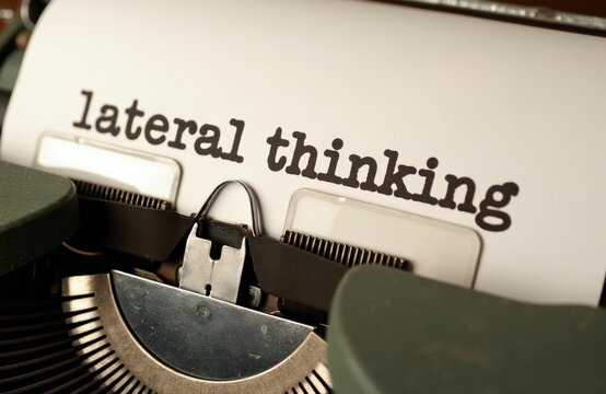 Close up view of vintage typewriter typing lateral thinking phrase on white paper sheet. Concept for creative strategy, problem solving skills shows black ink lettering on textured page. Antique