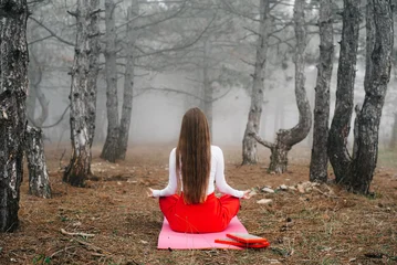 Fotobehang Lotusbloem Back view of a woman meditating in lotus pose in a misty forest  © komokvm