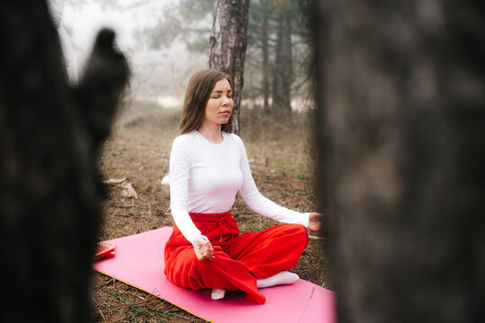 Woman meditating in lotus pose framed by trees in a foggy forest
