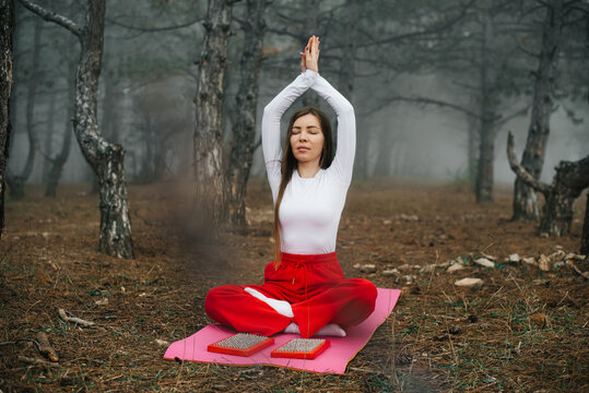 Woman meditating with raised hands in a foggy autumn forest