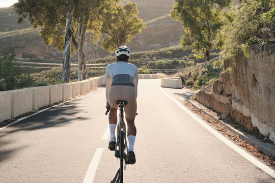 Rear view of a person cycling on a scenic road surrounded by hilly landscapes under warm sunlight. Capturing the essence of outdoor adventure, healthy lifestyle, and freedom on the open road.
