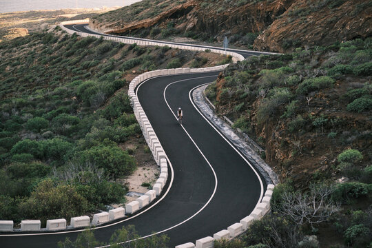 A lone cyclist navigates a dramatically winding mountain road, surrounded by rugged terrain and lush green shrubbery. Emphasizes endurance, freedom, and the beauty of outdoor adventure.