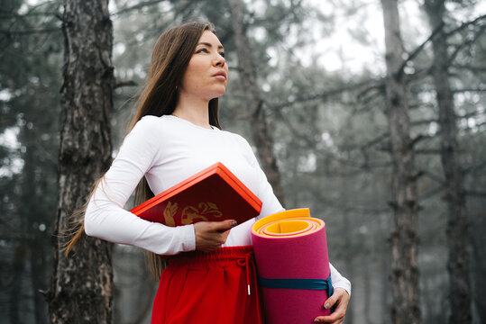 Portrait of a woman holding a yoga mat and sadhu boards in a forest