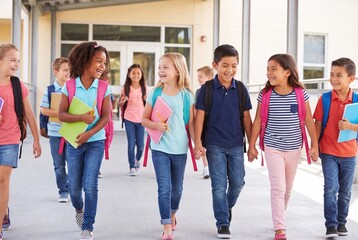 Obraz premium Diverse group of happy elementary school children walking together after school with backpacks and books.