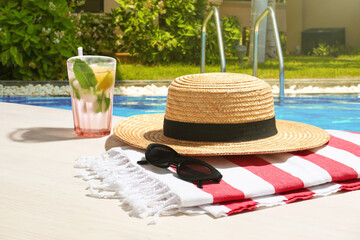 Obraz premium Sunglasses, straw hat, cocktail and towel by swimming pool