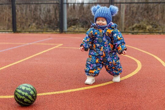 Toddler Walking Toward Ball on Outdoor Court in Winter Clothing