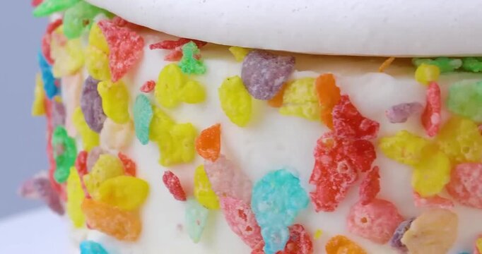White frosted cake decorated with colorful fruity cereal flakes close-up