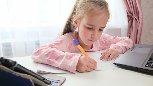 Child writing homework task at home with online learning setup