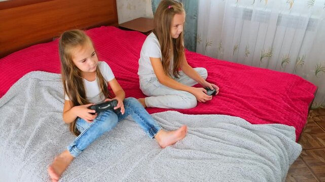 Carefree sisters playing online video game with joysticks in bedroom. Little girls relaxation after school