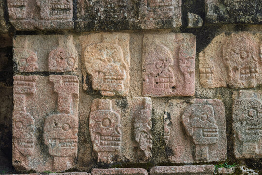 Close up of the pinkish stone skull carvings on the Tzompantli wall in Chichen Itza, Mexico